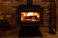 A lit wood stove over a brick background.