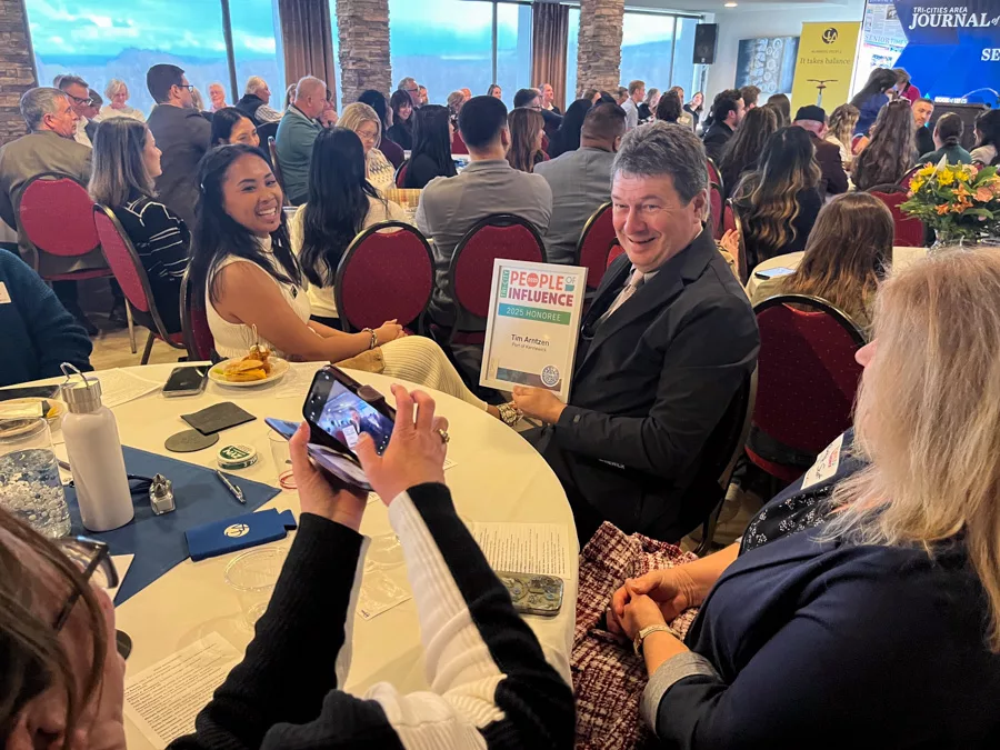 Tim Arntzen holding up his award at a table for a picture.