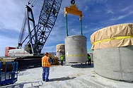 Workers lifting large concrete cylinders with a crane.