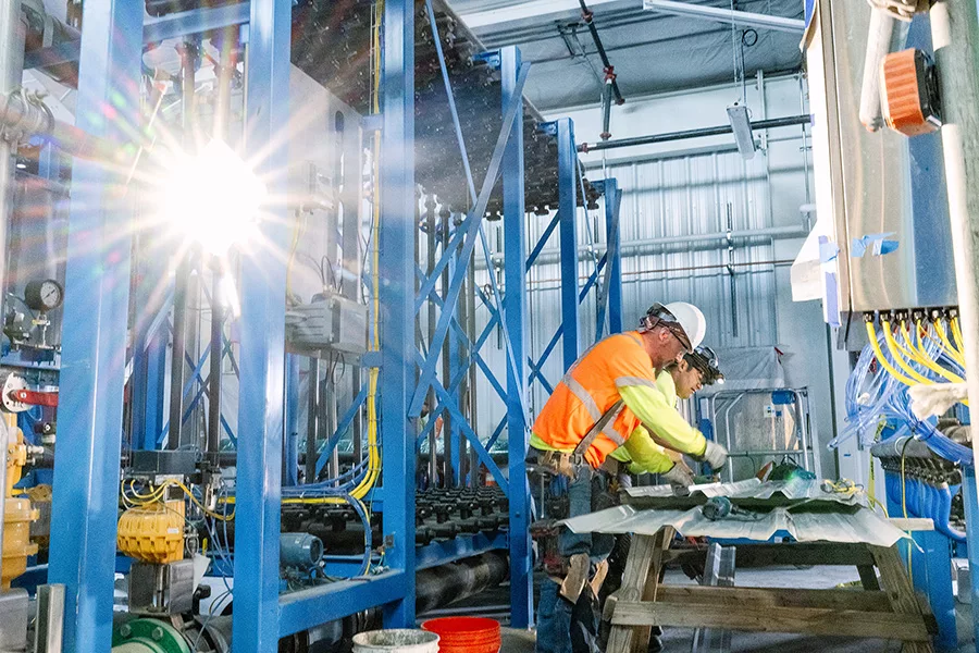 Workers inside a room wearing hard hats.