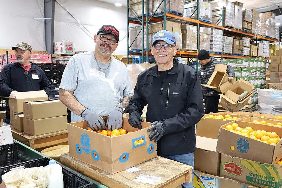 Two men with a box of oranges in a warehouse.