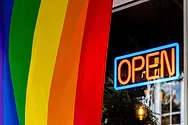 LGBTQ flag outside of a business with an open sign.
