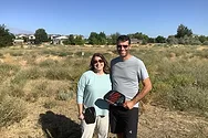 Two people in a field with pickle ball paddles.