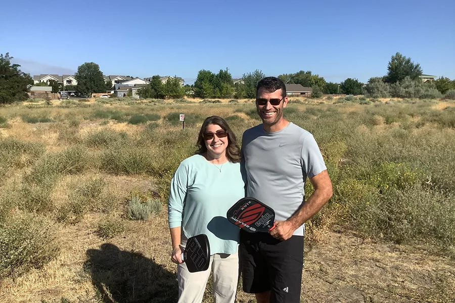 Two people in a field with pickle ball paddles.