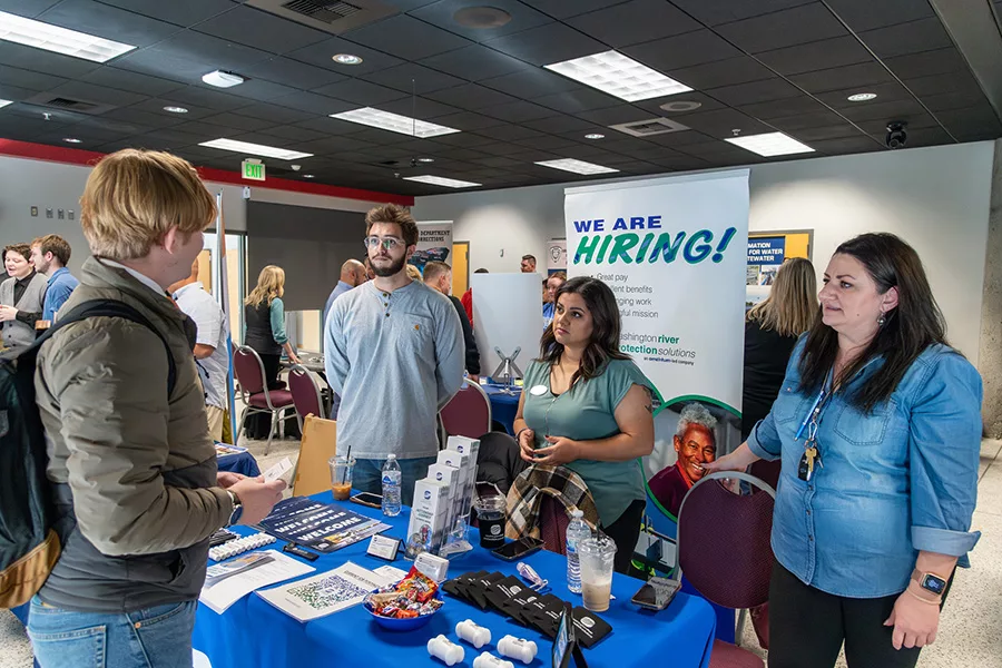 A student talking to people behind a booth at a job fair.