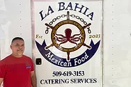 A man standing next to a food truck with an octopus logo. The logo reads, "La Bahia Mexican Food"
