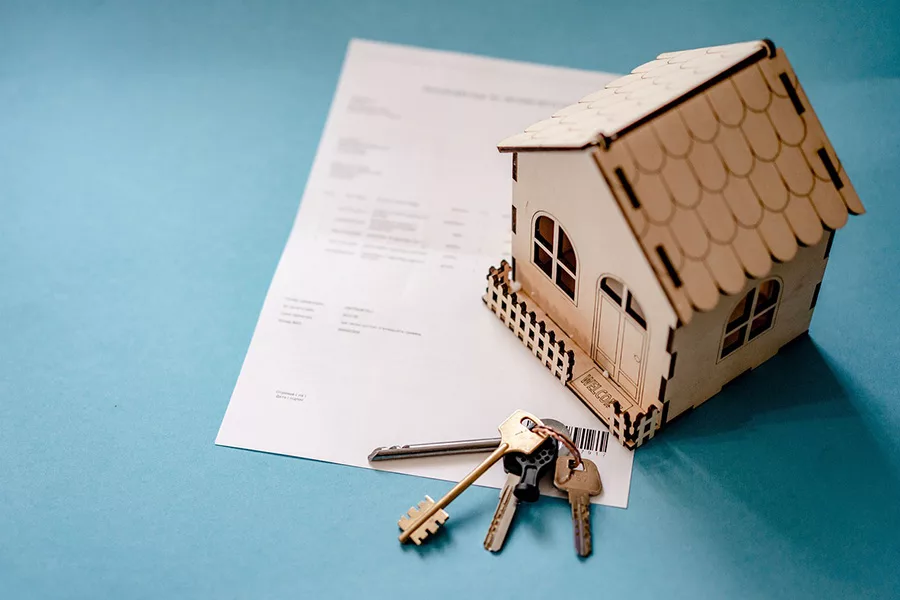 A little wooden house model on a piece of paper with some keys.