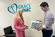 Two people near a wall that says "Grace Clinic". One person is holding a binder.