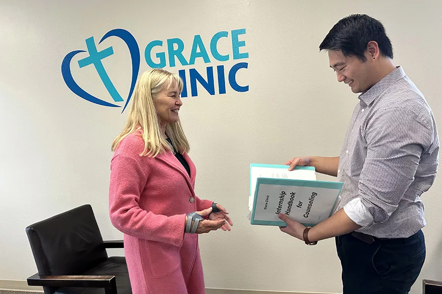 Two people near a wall that says "Grace Clinic". One person is holding a binder.