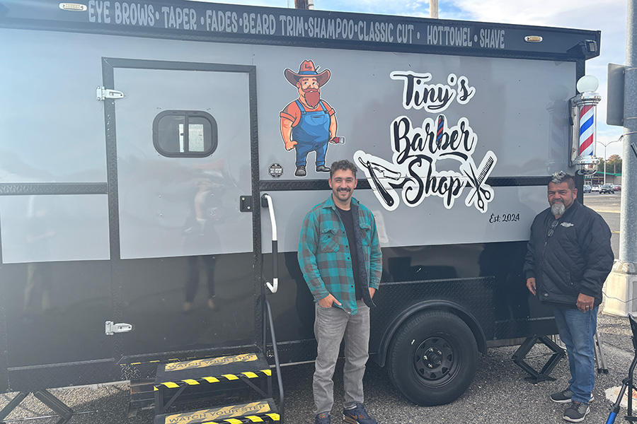 Two people standing by a truck that says "Tiny's Barber Shop".