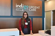 Woman stands behind a counter near a sign that says, "Indigo Urgent Care".