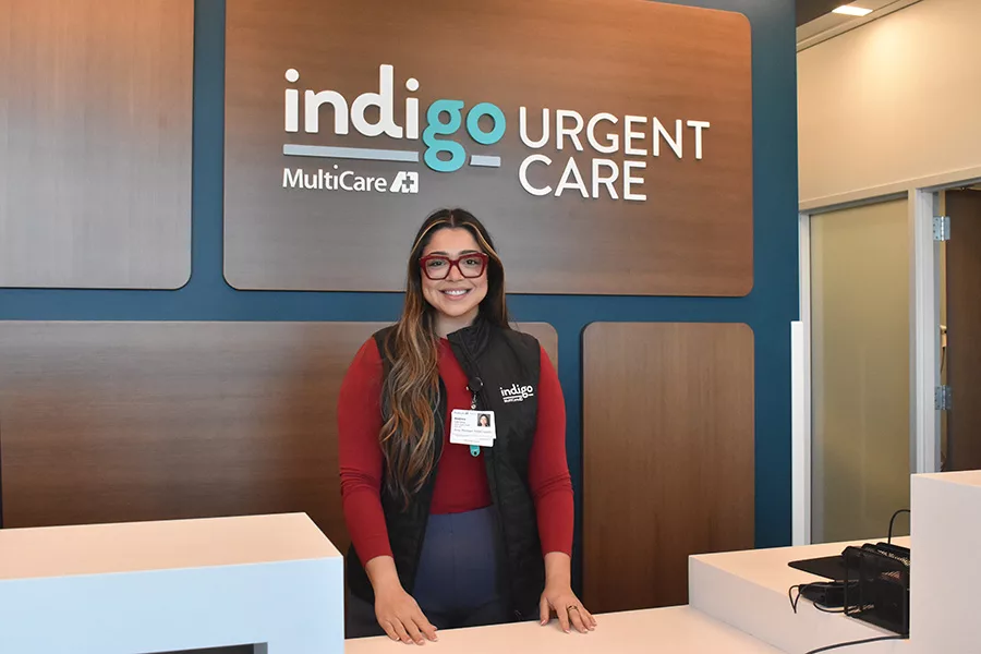 Woman stands behind a counter near a sign that says, "Indigo Urgent Care".