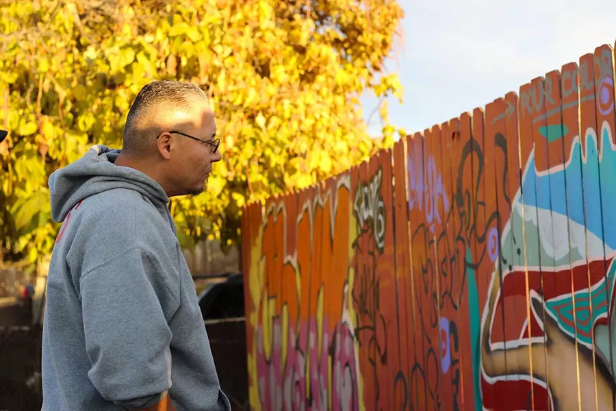 Man viewing a fence with graffiti.