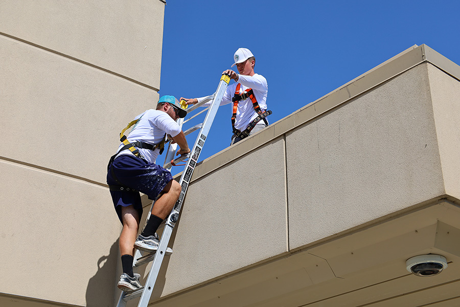 A man climbing a ladder while another holds it.