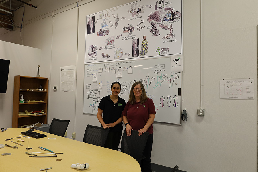 Two women standing by a large whiteboard.