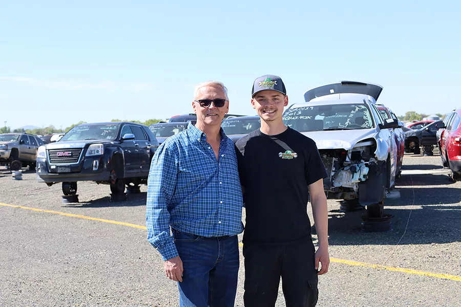 A father and son standing in a lot with wrecked cars.