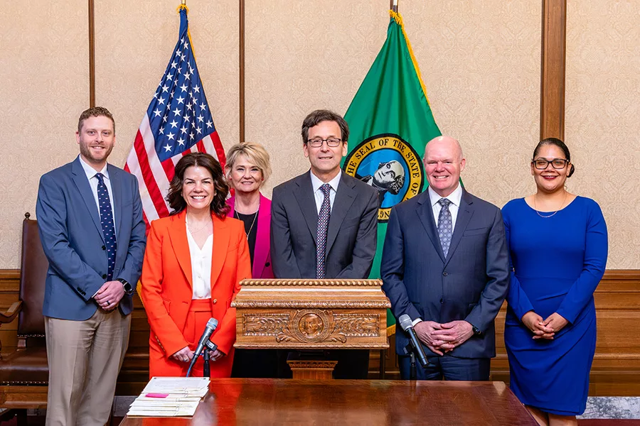 People standing behind a podium near U.S. and Washington flags.