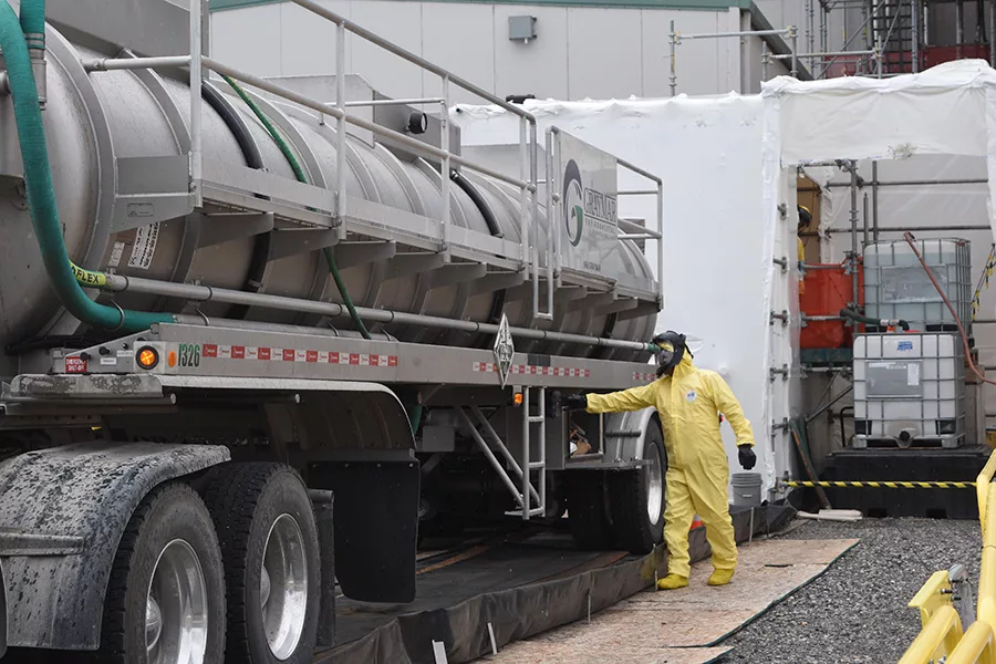 A worker in a hazard suit near a tanker truck.