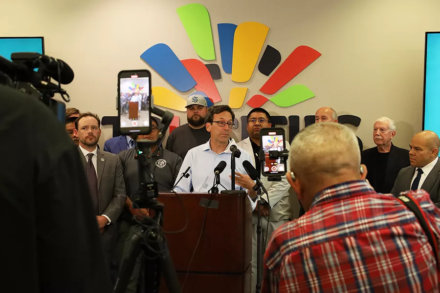 Governor speaking behind a podium with people behind him and cameras in the foreground.