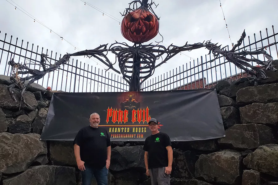 Two people and a giant pumpkin creature display next to a sign that says "Pure Evil".