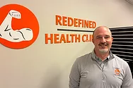 A man standing next to a sign that says, "Redefined Health Clinic".