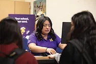 A woman behind a bank counter helping two customers.