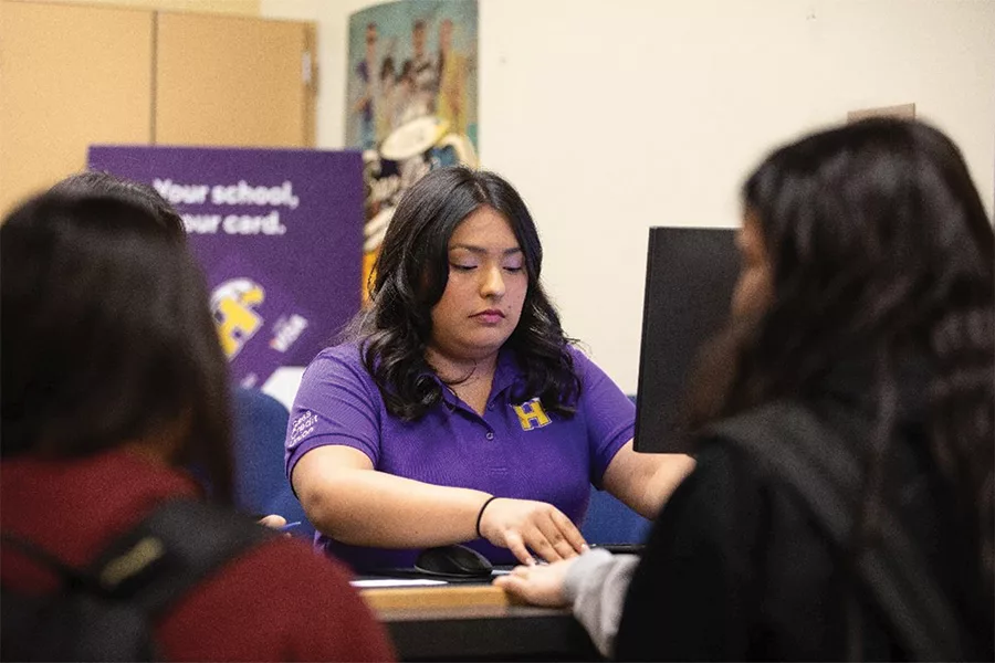 A woman behind a bank counter helping two customers.