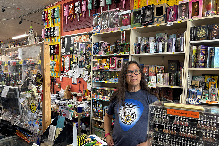 A man standing behind a register near a wall of various knick-knacks.