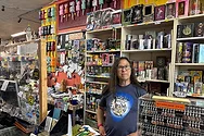 A man standing behind a register near a wall of various knick-knacks.