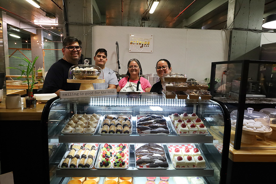 People standing behind a case of baked goods.