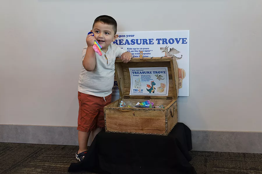 A kid standing next to a treasure chest with a sign that says, "Treasure Trove".