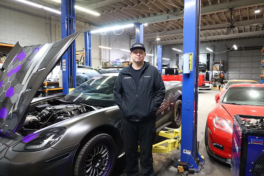 Man standing next to a car in a shop.
