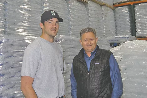 Two people in a freezer full of bags of ice.