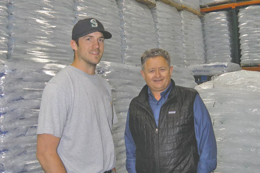 Two people in a freezer full of bags of ice.