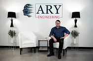 Man sitting in a chair next to a sign that says ARY Engineering.