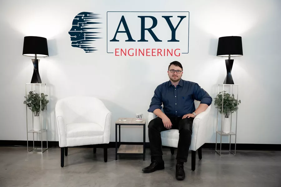 Man sitting in a chair next to a sign that says ARY Engineering.