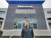Person standing outside of a building that says, "Bluecarrot".