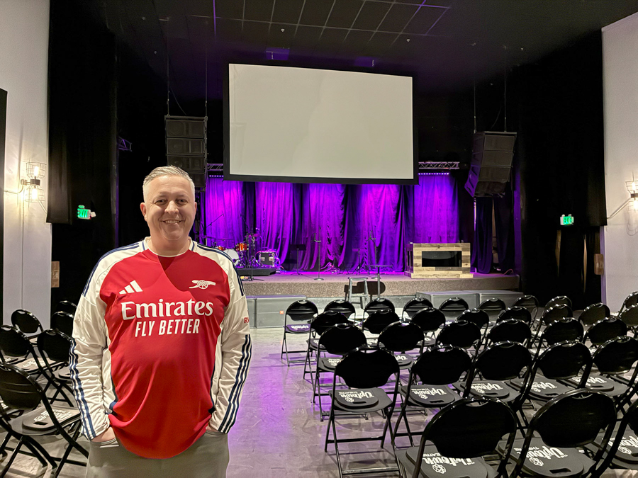 Person standing in a room with chairs and a stage.
