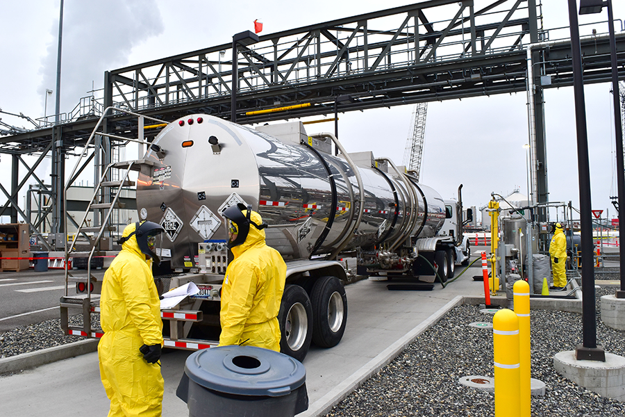People in hazard suits near a fluid truck.