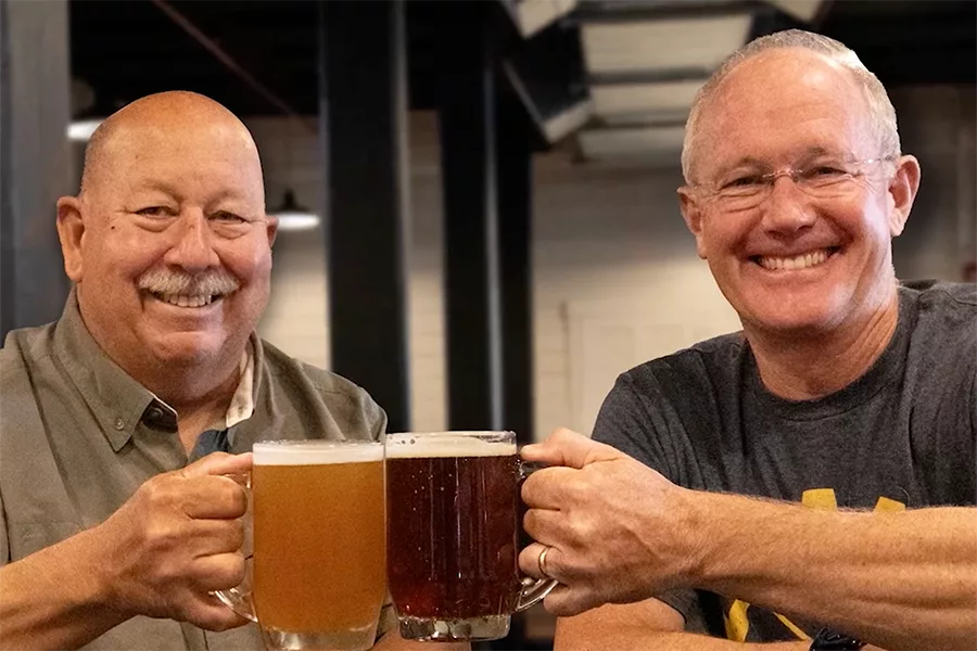 Two men cheering beer mugs.