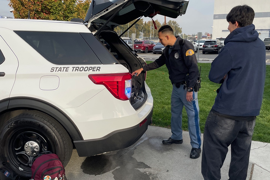 People inspecting the trunk of a state trooper vehicle.
