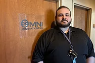 Man stands by a sign that says, "Omni Innovations".