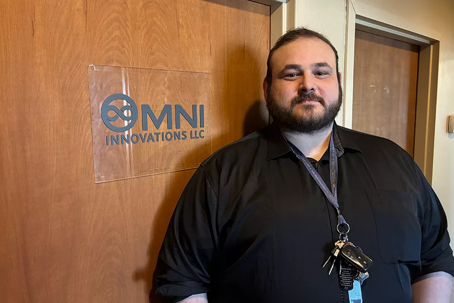 Man stands by a sign that says, "Omni Innovations".