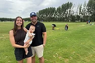 Two people and a baby near a golf driving range.