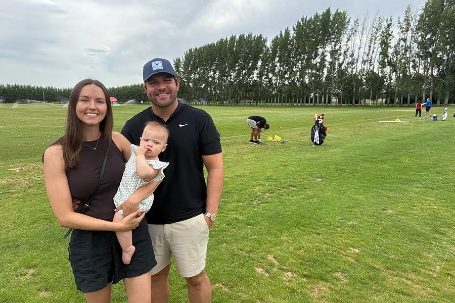 Two people and a baby near a golf driving range.