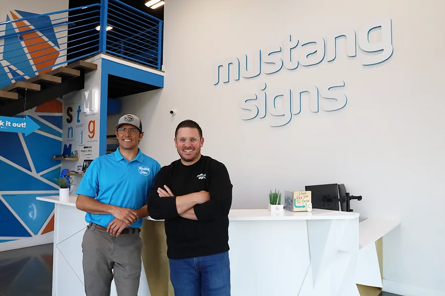 Two men by the Mustang Signs logo.