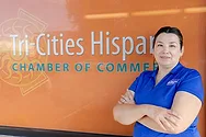 A women with an SBDC shirt in front of the Tri-Cities Hispanic Chamber of Commerce sign.