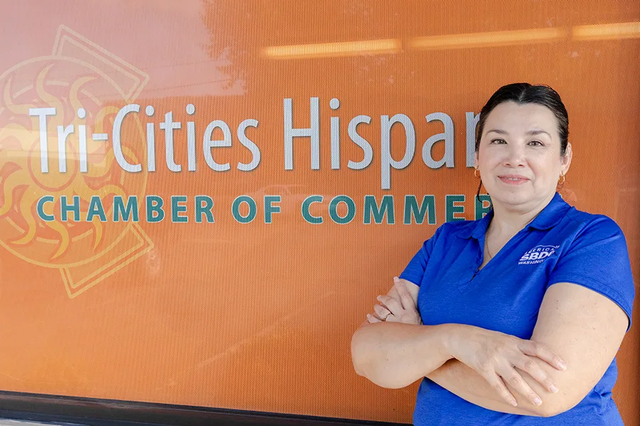 A women with an SBDC shirt in front of the Tri-Cities Hispanic Chamber of Commerce sign.