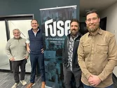 Four men standing near a sign that says, "Fuse".