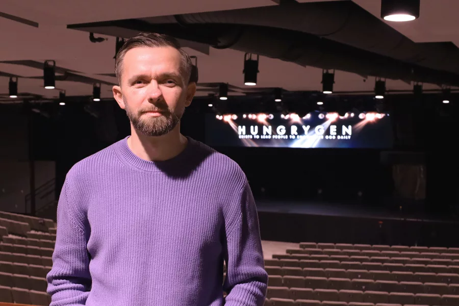 A man standing with a stage in the background that reads, "Hungry Gen".